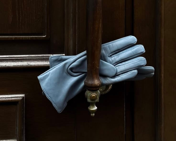 A pair of light blue leather gloves draped over a dark brown wooden door handle with brass hardware.