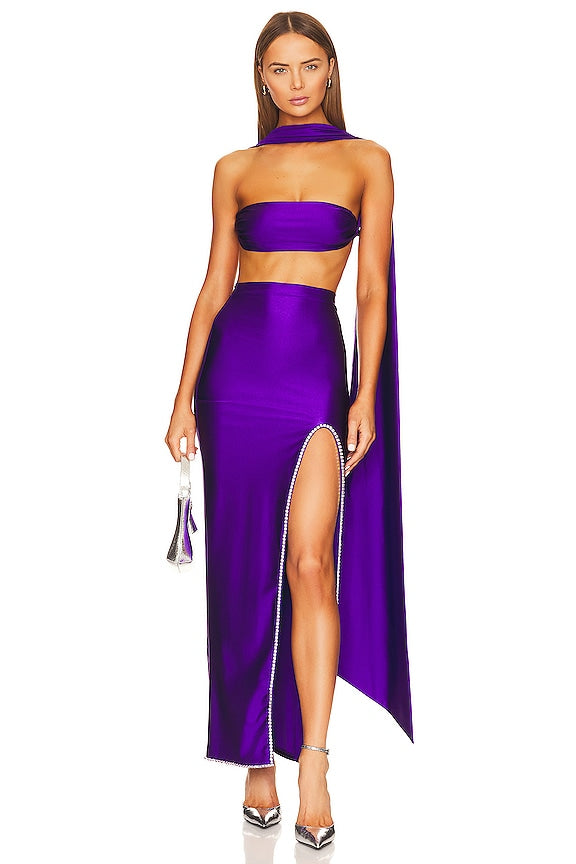 Woman wearing a purple two-piece outfit with a slit skirt on a white background