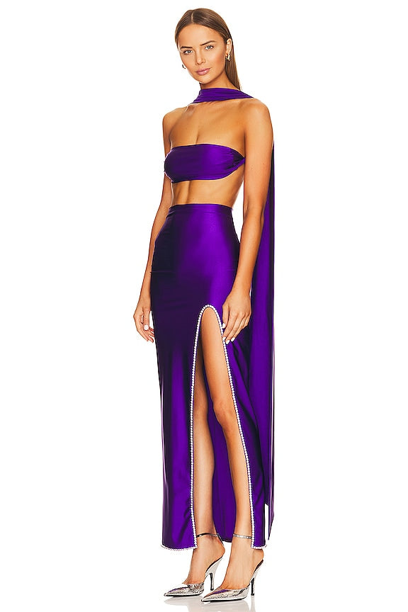 Woman wearing a purple two-piece outfit with a slit skirt on a white background